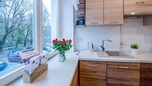 A modern kitchen with wooden cabinets, a white countertop, a sink, and a window with a view of trees and parked cars.