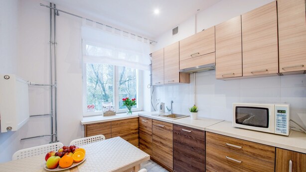 A modern kitchen with wooden cabinets, a microwave, and a table with fruit.
