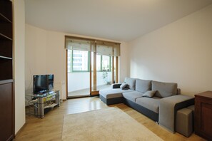 A modern living room with a grey sectional sofa, a glass TV stand, and a large sliding glass door leading to a balcony.