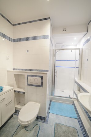 A bathroom with a toilet, sink, shower, and tiled walls.