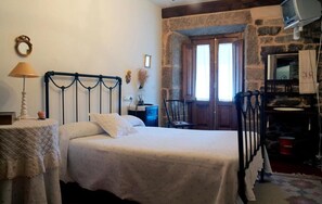Une chambre à coucher avec un lit, une table de chevet, une lampe, une chaise, un téléviseur et un mur en pierre.