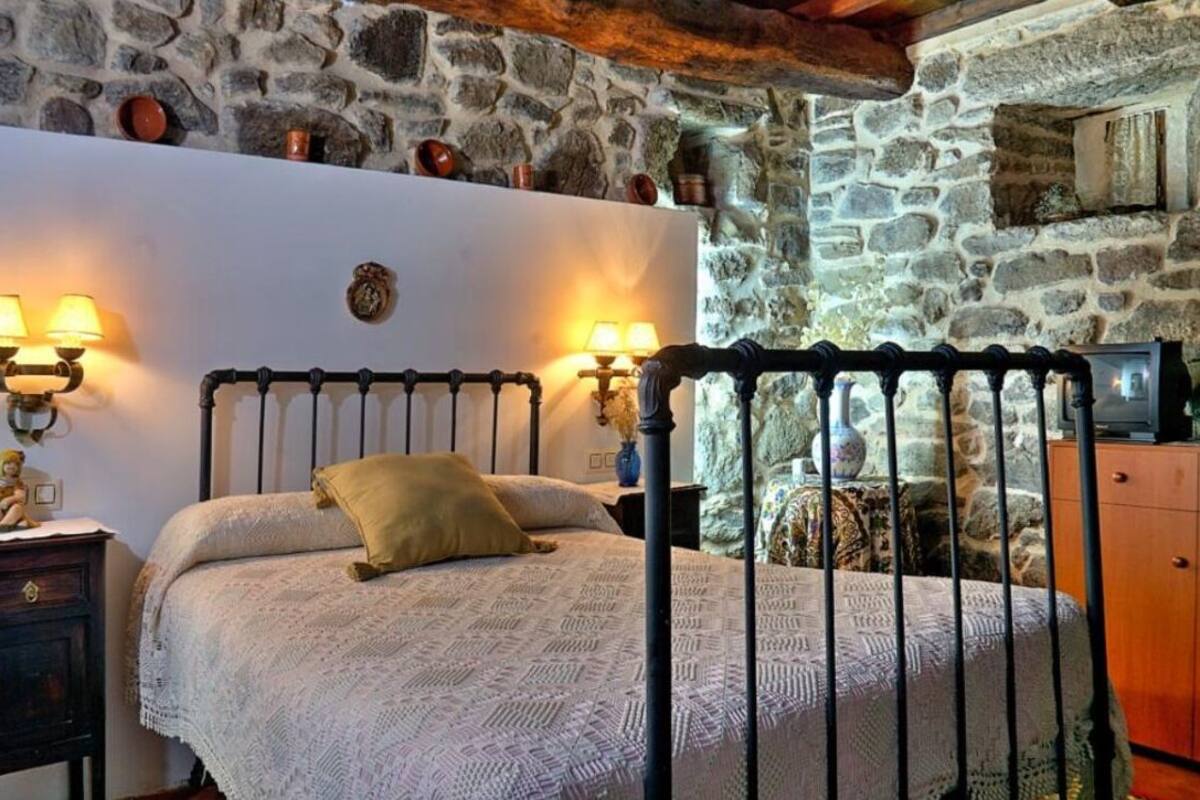 A bedroom with a stone wall, a bed with a headboard, bedside lamps, and a wooden cabinet.
