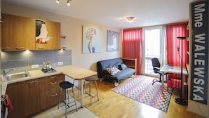 A compact living space with a kitchenette, a sofa, a desk, and a large window with red curtains. - Art&Apart (Warsaw)