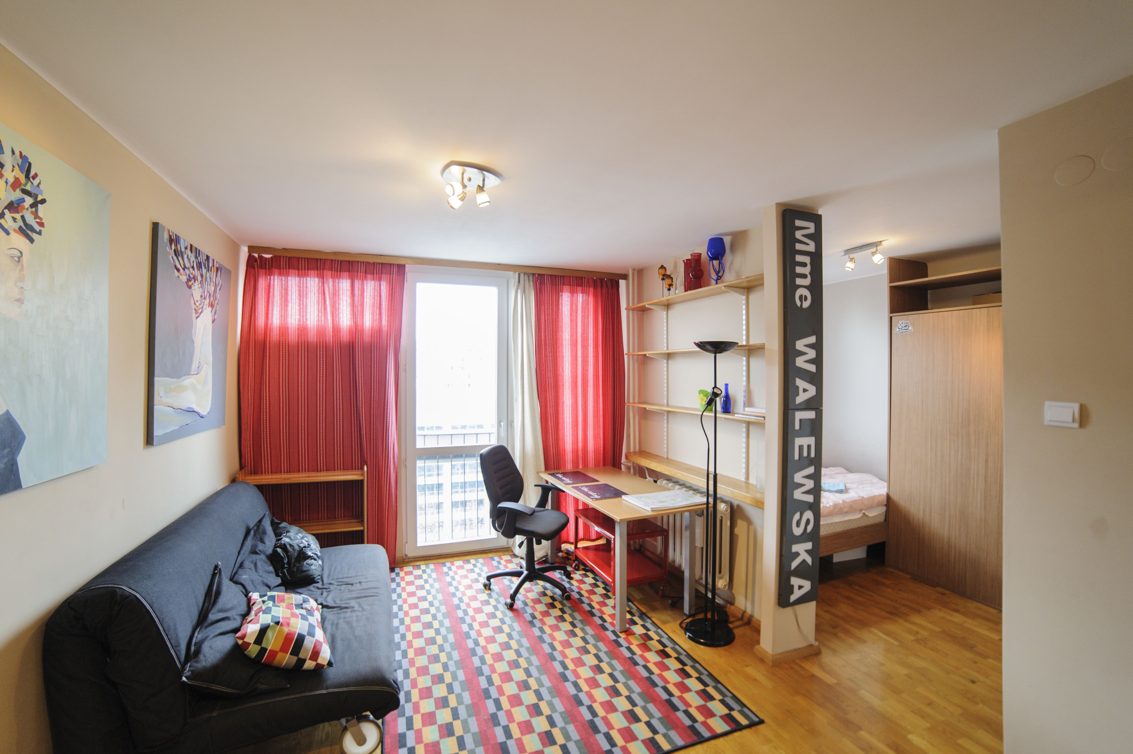 Una habitación pequeña con cama, escritorio, silla y una alfombra colorida.