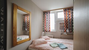 A bedroom with a bed, a mirror, a window with curtains, and a radiator. - Art&Apart (Warsaw)