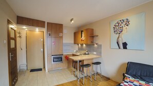 A compact kitchen with wooden cabinets, a built-in oven, a sink, and a bar stool area. - Art&Apart (Warsaw)