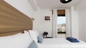A hotel room with a large bed, a headboard, a small table, a chair, and a window with curtains. - LV Premier Marques - MQ2 (Porto)