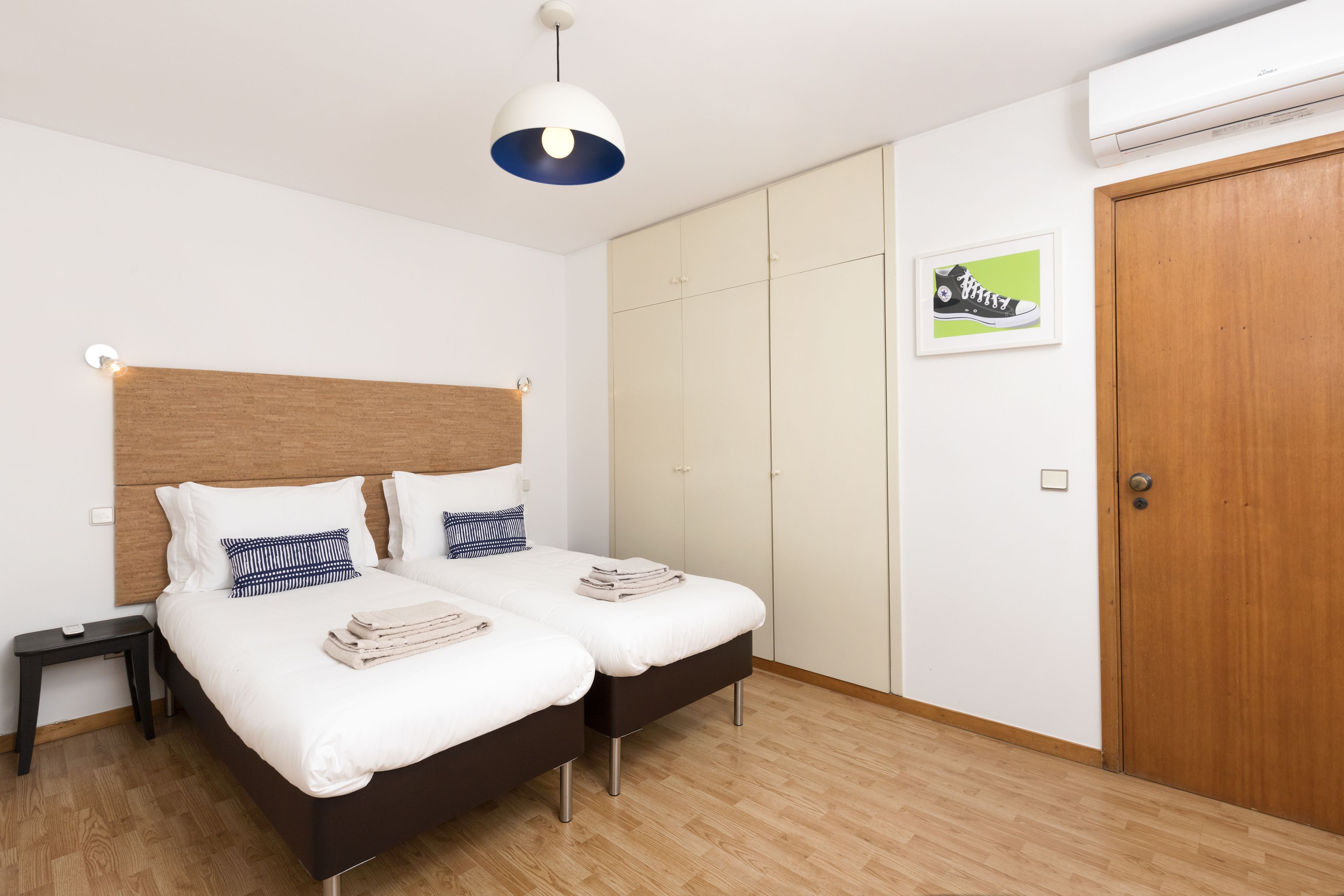 A bedroom with two beds, a wooden headboard, a wardrobe, and a framed picture on the wall.