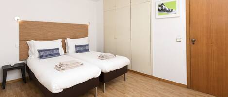 A bedroom with two beds, a wooden headboard, a wardrobe, and a framed picture on the wall.