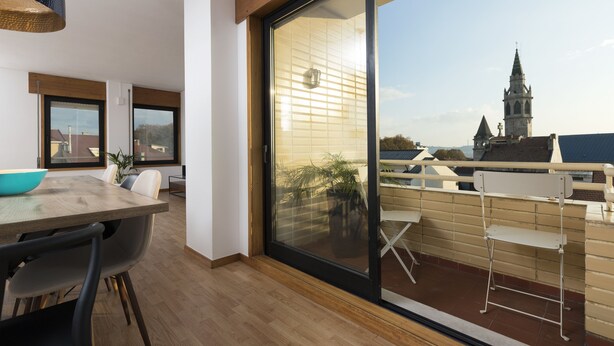 A modern interior with a dining area, a sliding glass door leading to a balcony, and a view of a church tower. - LV Premier Marques - MQ2 (Porto)