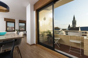 Un interior moderno con comedor, una puerta corrediza de vidrio que da a un balcón y vista a una torre de iglesia.