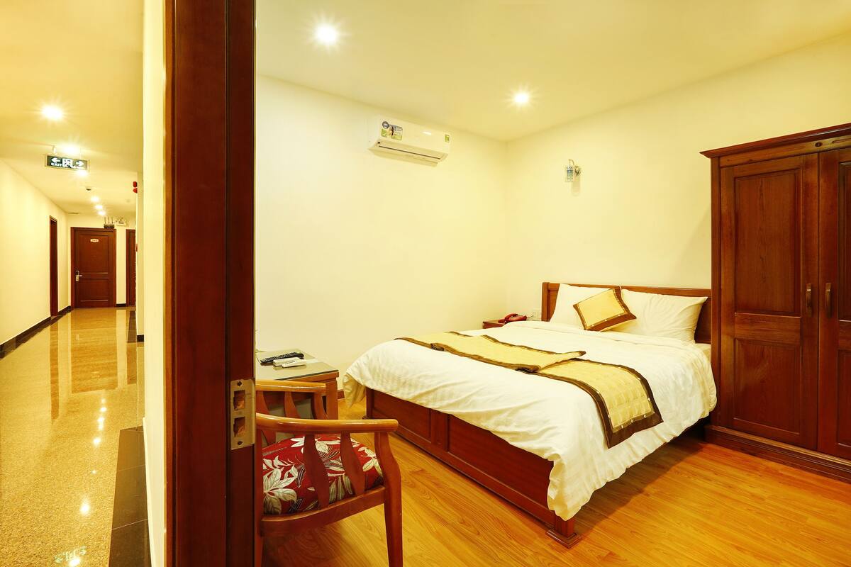 A hotel room with a wooden bed, a wooden wardrobe, a wooden chair, and a small table.