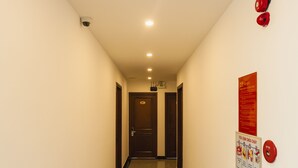 Um corredor com piso polido, uma câmera de segurança instalada no teto e um alarme de incêndio na parede.