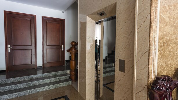 Um hall com piso de mármore, portas de madeira, uma escadaria e uma parede de mármore com uma estátua.