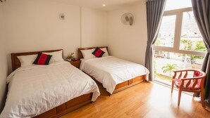 Quarto de hotel com duas camas, piso de madeira, janela com cortinas e uma cadeira.