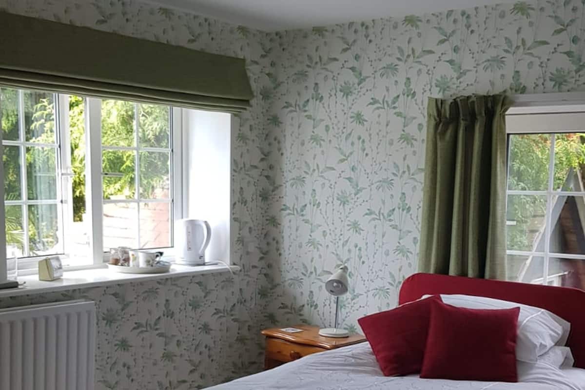 A bedroom with a bed, a nightstand, a radiator, and two windows with curtains.