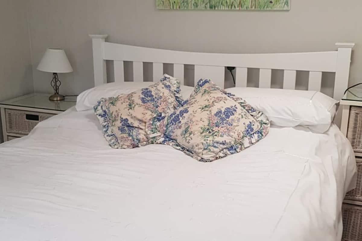 A neatly made bed with floral pillows, a white headboard, and a painting of flowers on the wall.