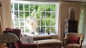 Un salon spacieux avec une grande fenêtre, un fauteuil rouge, un canapé à motifs et un fauteuil ancien.