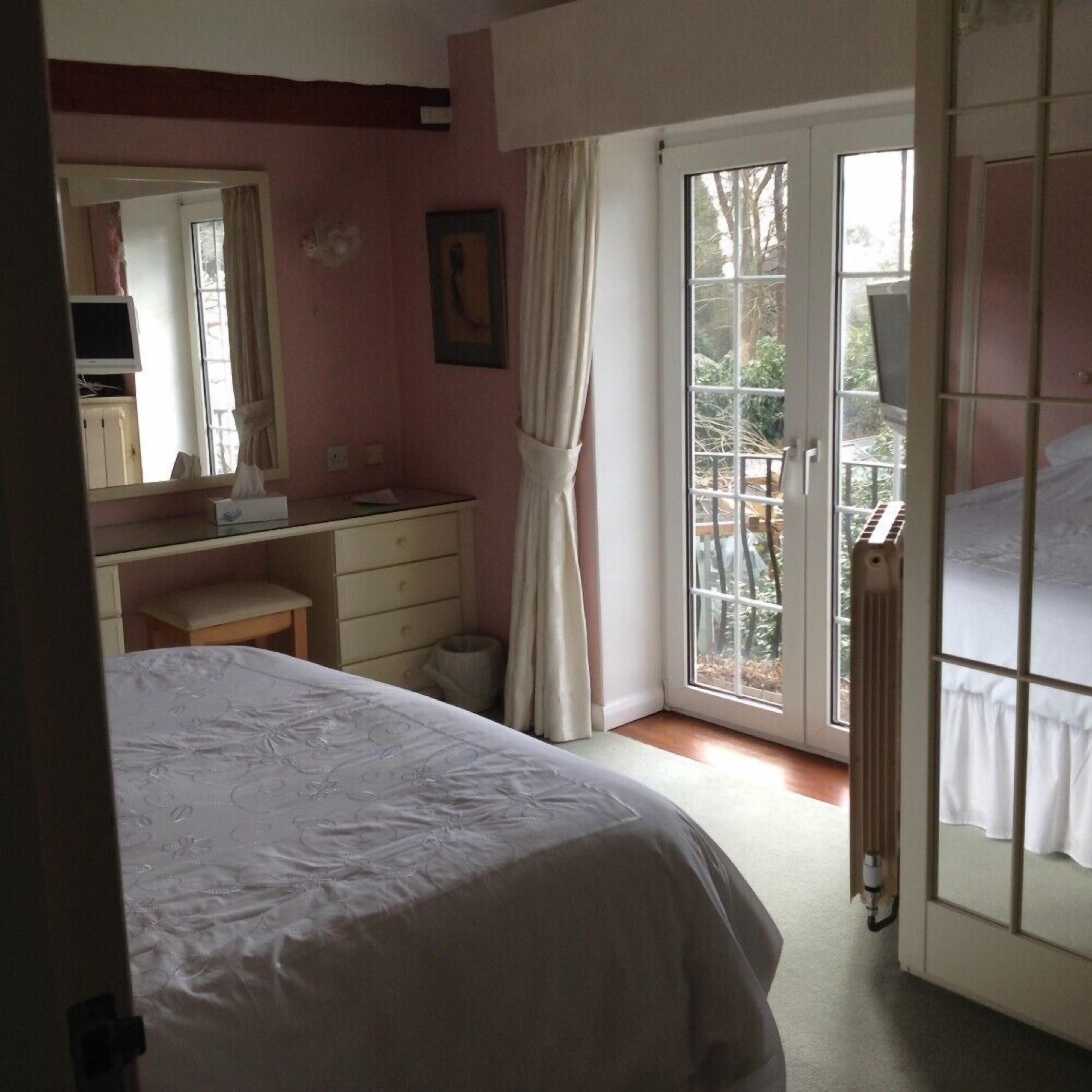 A bedroom with a bed, a dresser, a desk, a mirror, and a window with a view of trees.