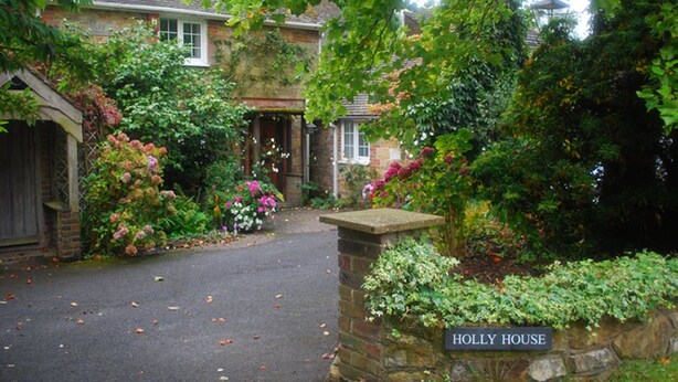Une maison traditionnelle en pierre, appelée « Holly House », avec une allée pavée et un jardin luxuriant.