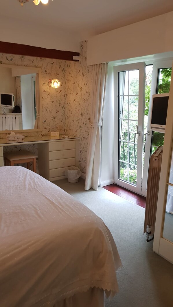 A bedroom with a bed, a dresser, a mirror, a television, and a sliding glass door leading to a balcony.