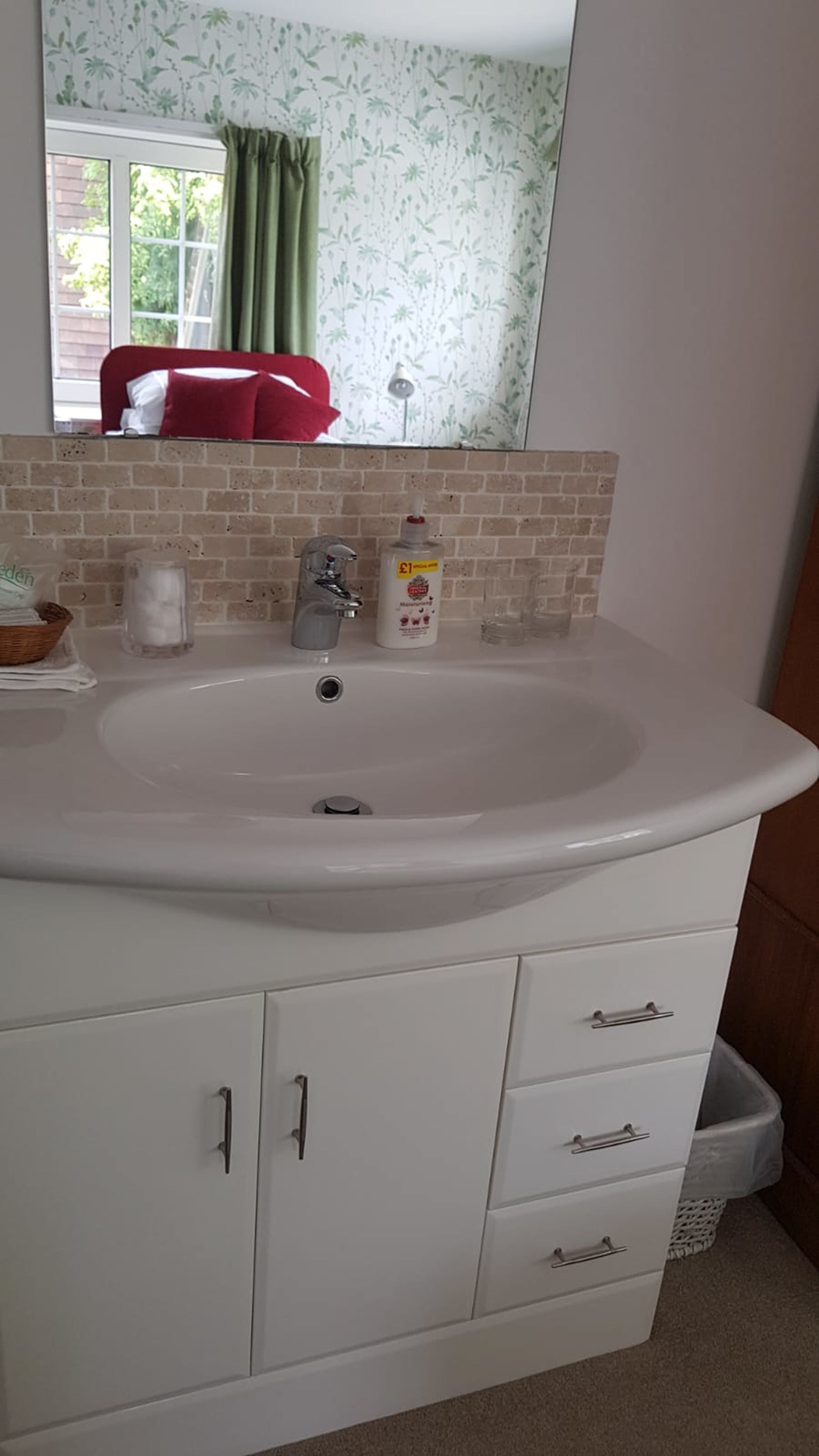 A bathroom with a white sink, a mirror, and a window with green curtains.