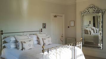 A bedroom with a white bed, a chandelier, a large mirror, and a door.