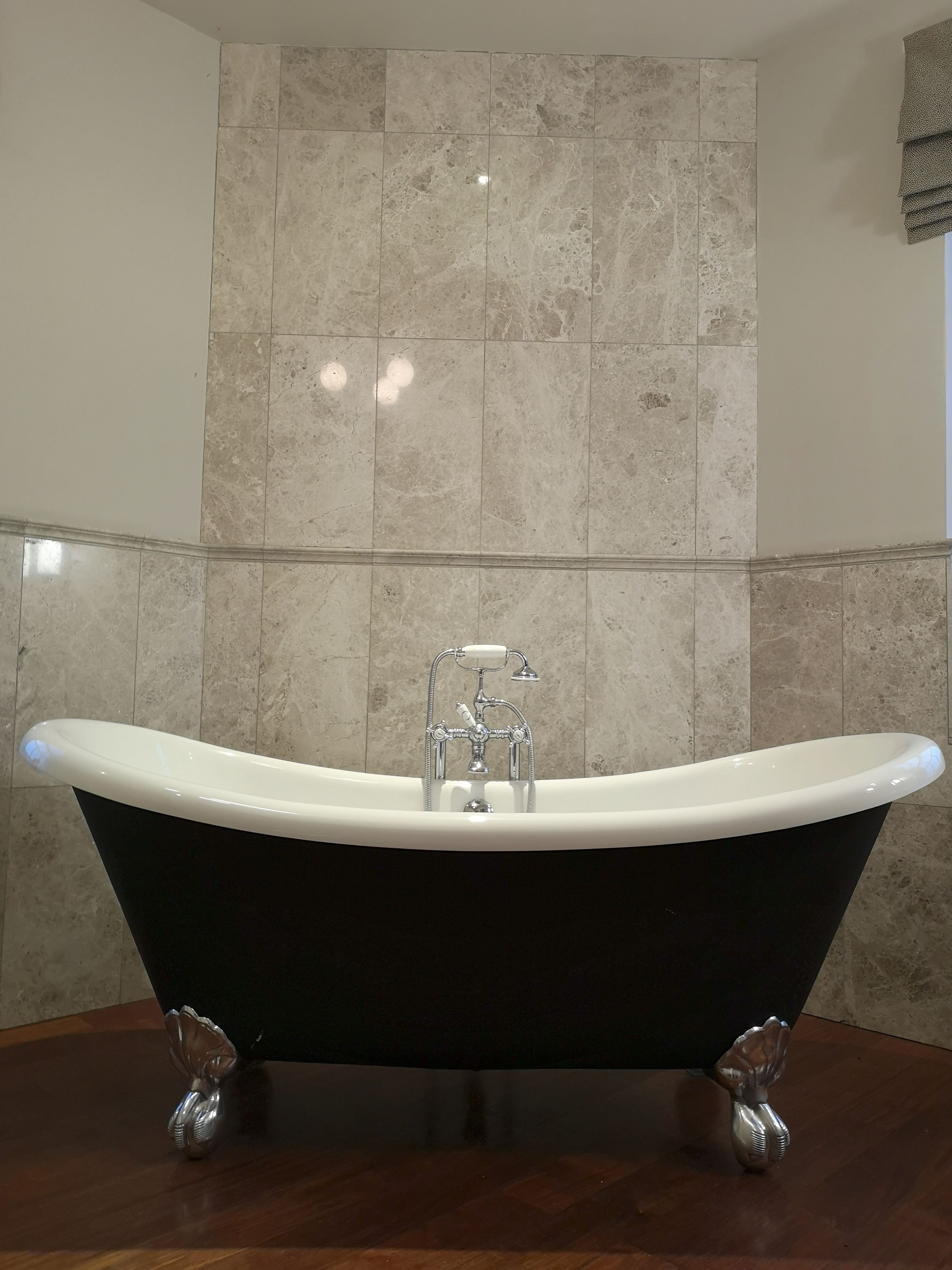 A modern bathroom with a freestanding bathtub, marble tiles, and a wooden floor.