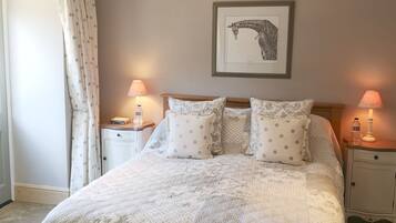 A neatly made bed with a floral-patterned duvet and matching pillows, flanked by two bedside tables with lamps, a framed giraffe artwork on the wall, and a large window with curtains.