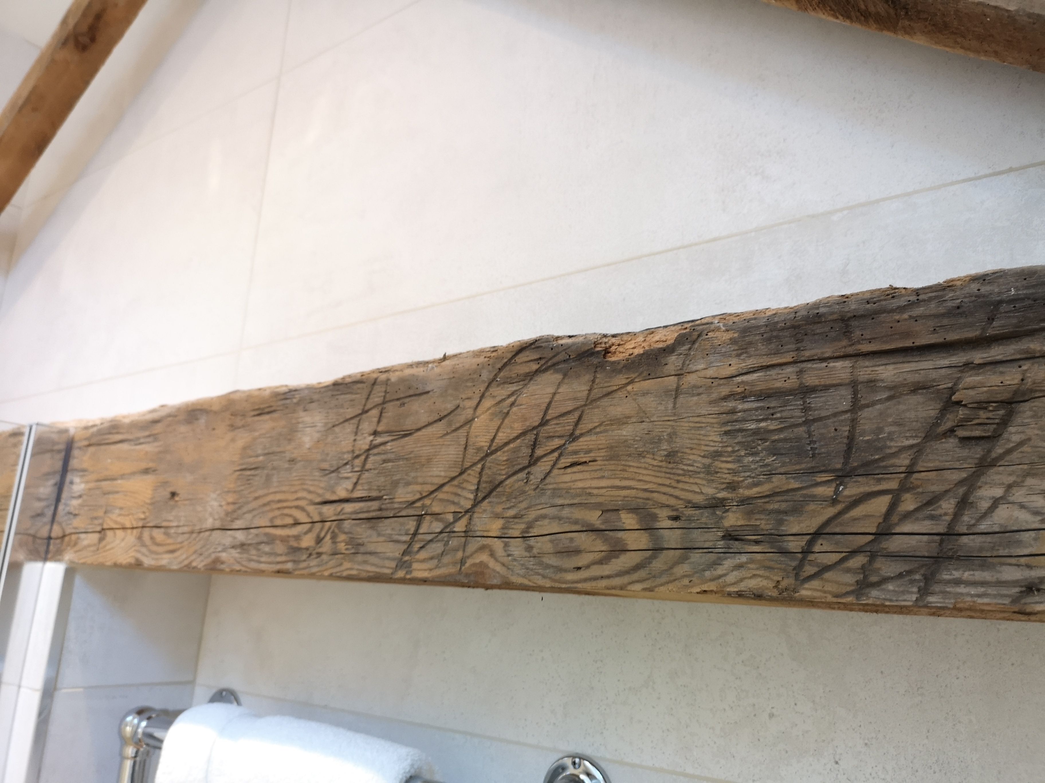 A bathroom with a wooden beam above the sink and a white tiled wall.