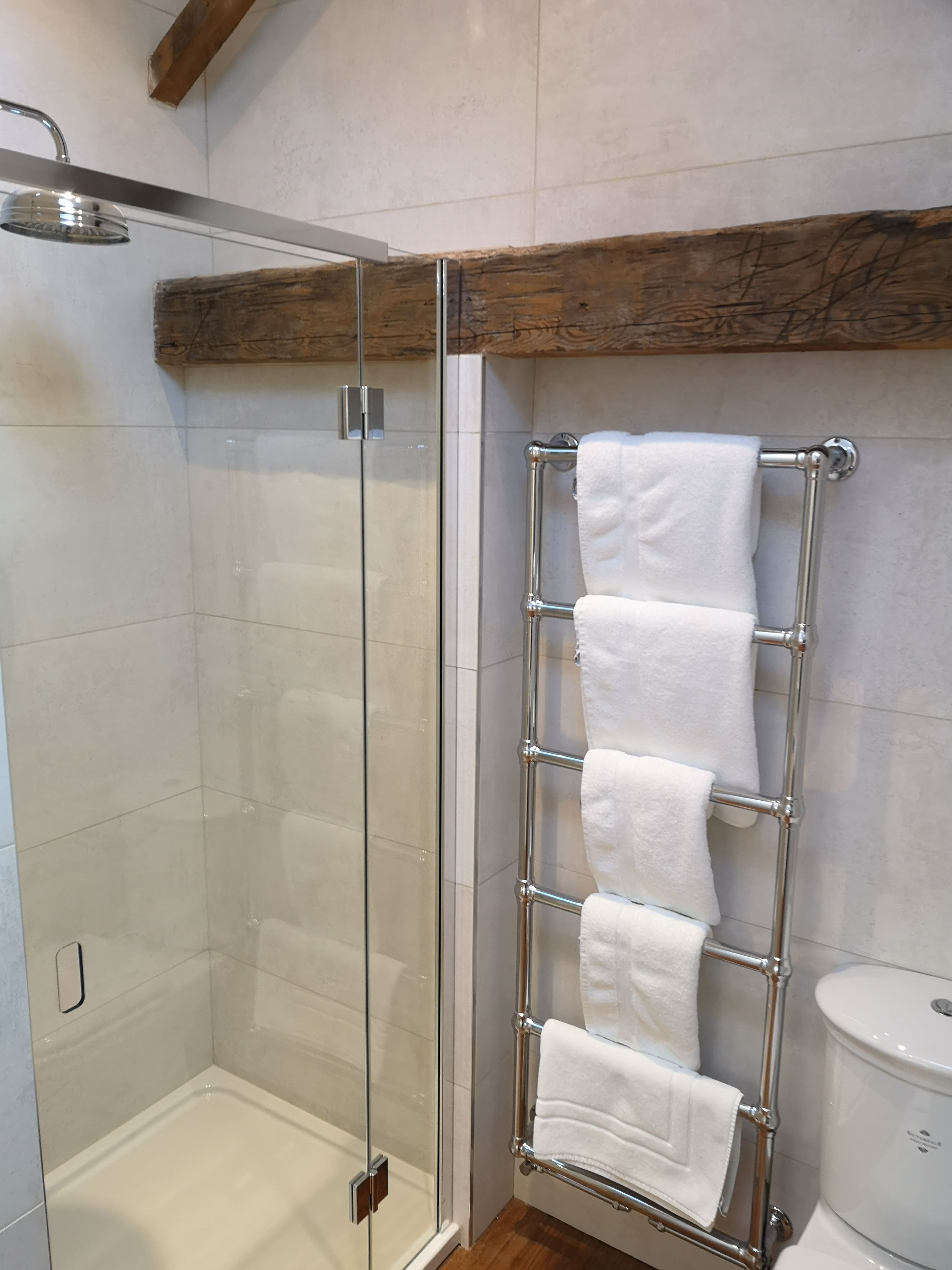 A glass-enclosed shower with a chrome towel rack holding several white towels.