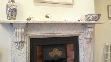 A marble fireplace with a black mantle, a framed floral artwork above it, and a vase with a floral design on the mantel.