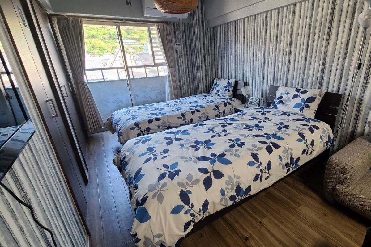 Ein Zimmer mit zwei Betten, Holzboden und Blick auf Grünfläche.