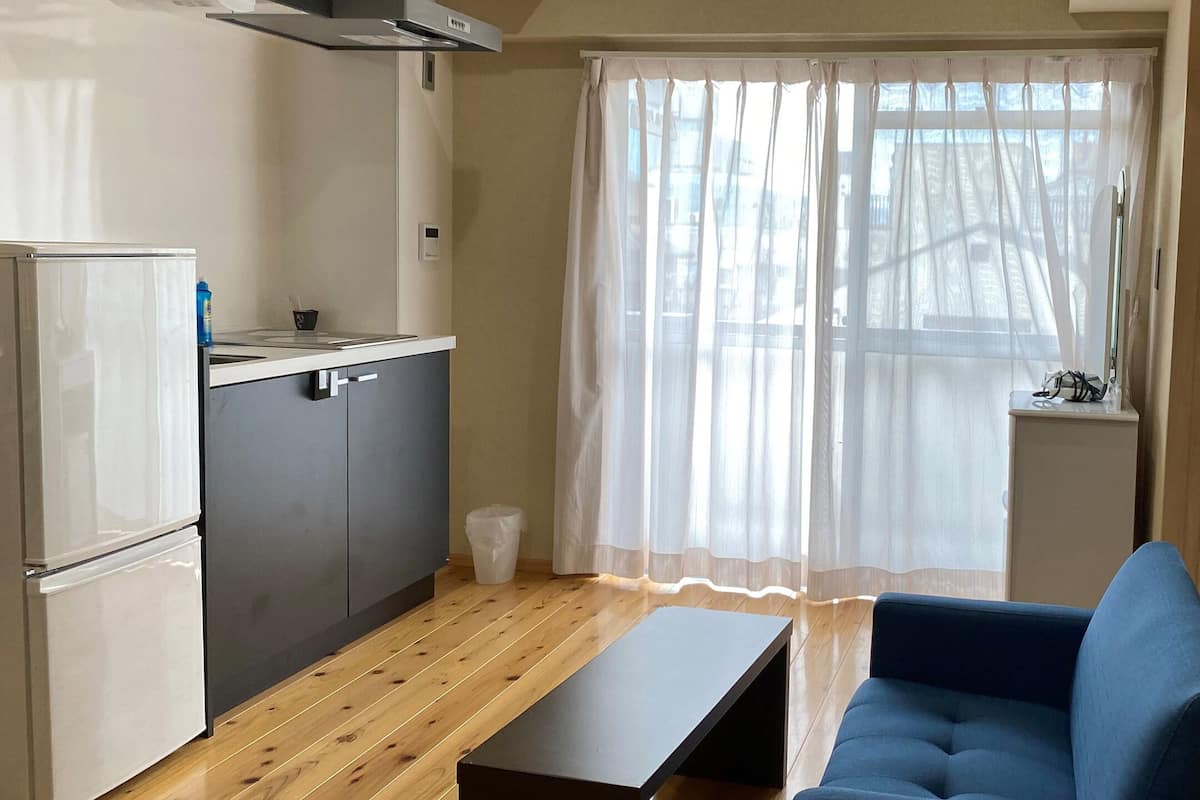 Eine kleine Küche mit Kühlschrank, Spüle und einem Fenster mit transparenten Vorhängen.