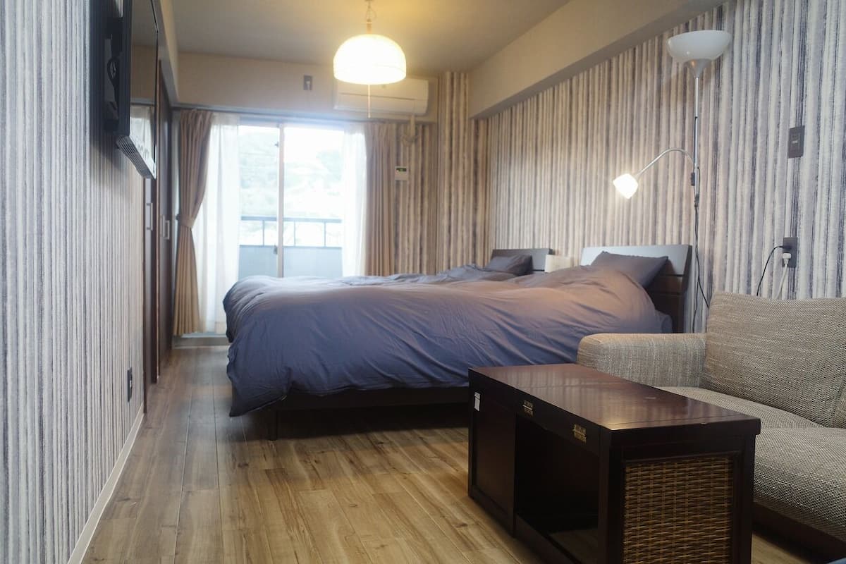 Een slaapkamer met een bed, een bank, een kleintje tafeltje en een raam met gordijnen.