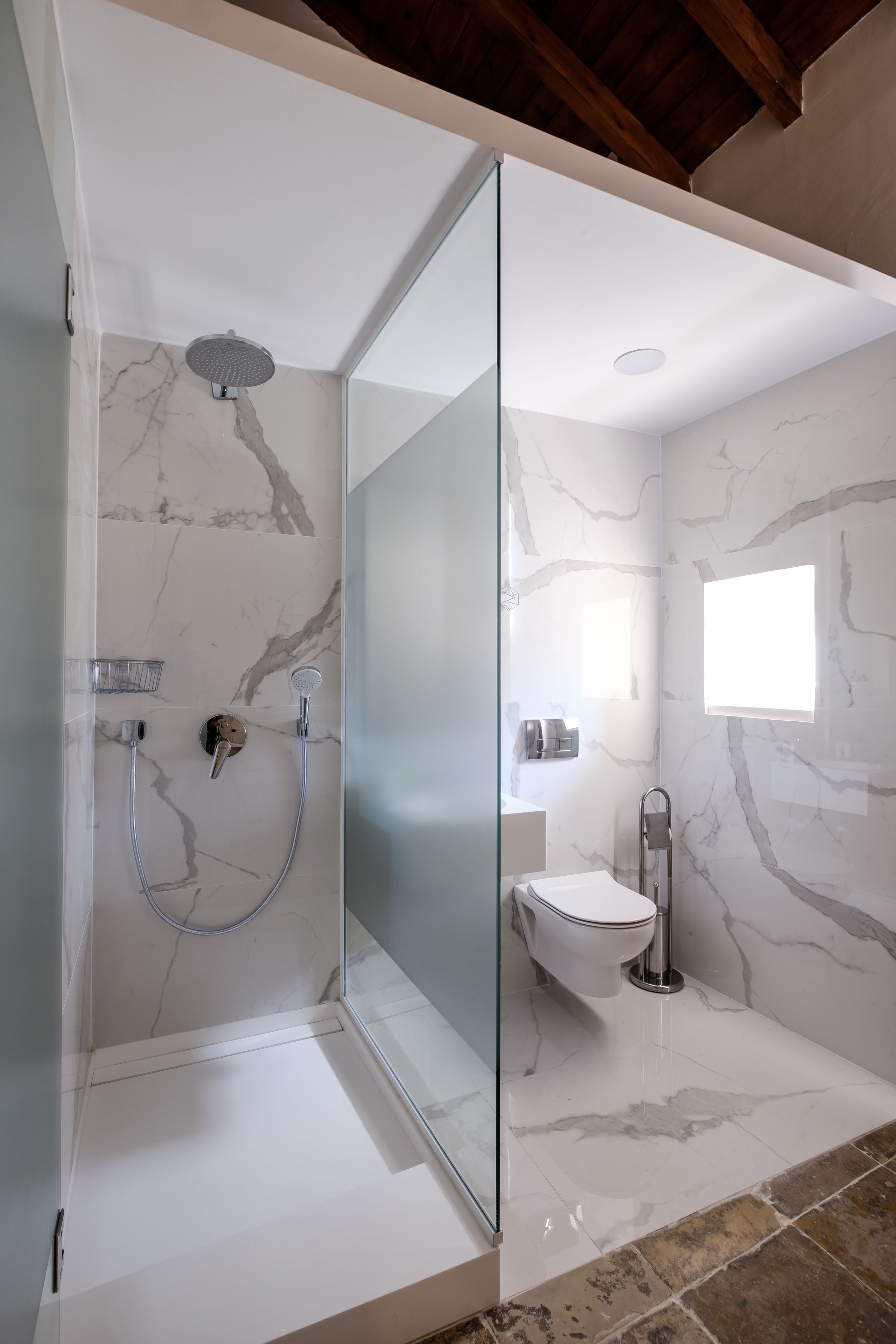 Un baño moderno con ducha de vidrio, paredes de mármol y lavamanos blanco.