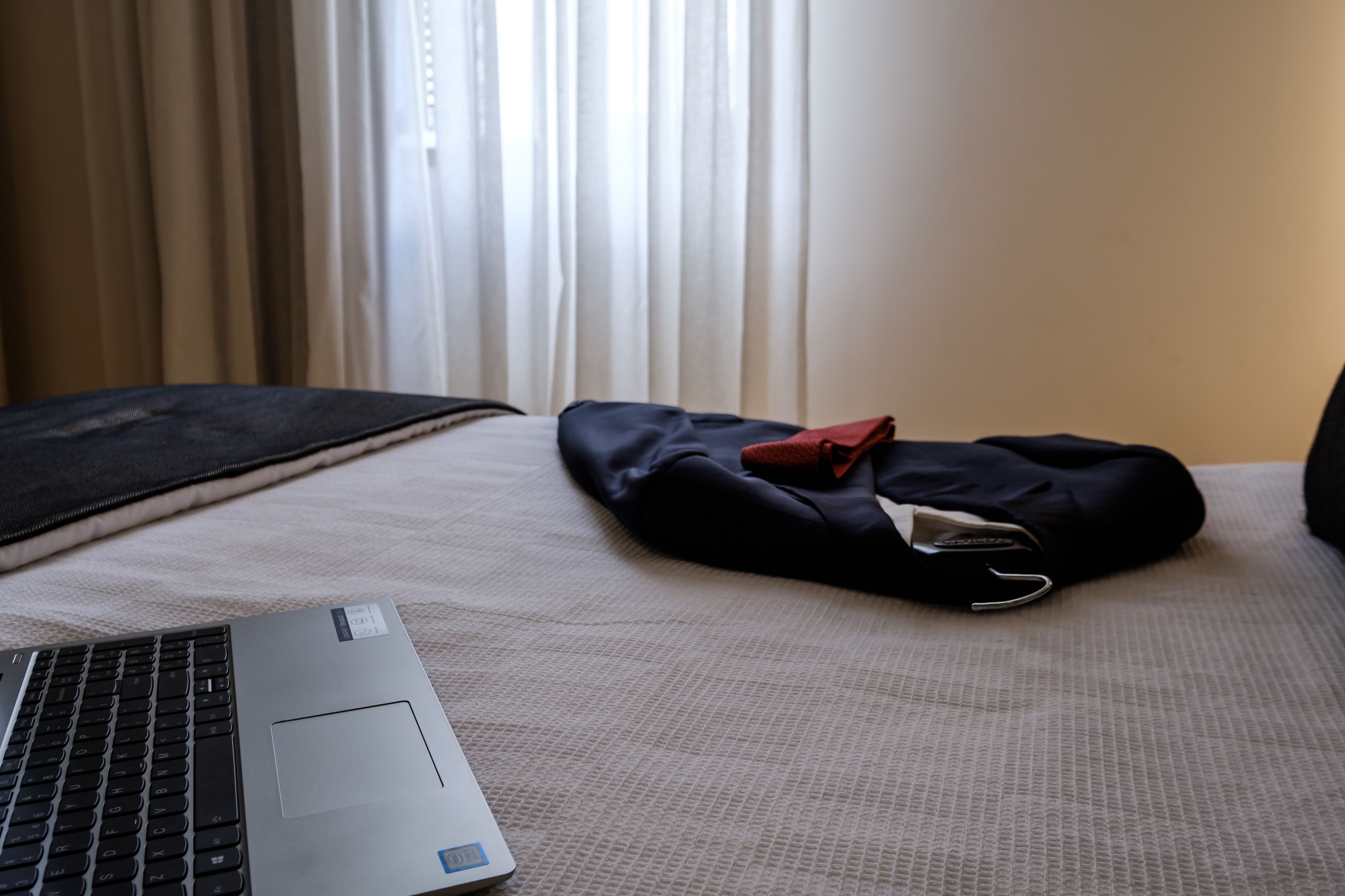 Um laptop sobre a cama, com uma bolsa preta e um objeto vermelho em cima.