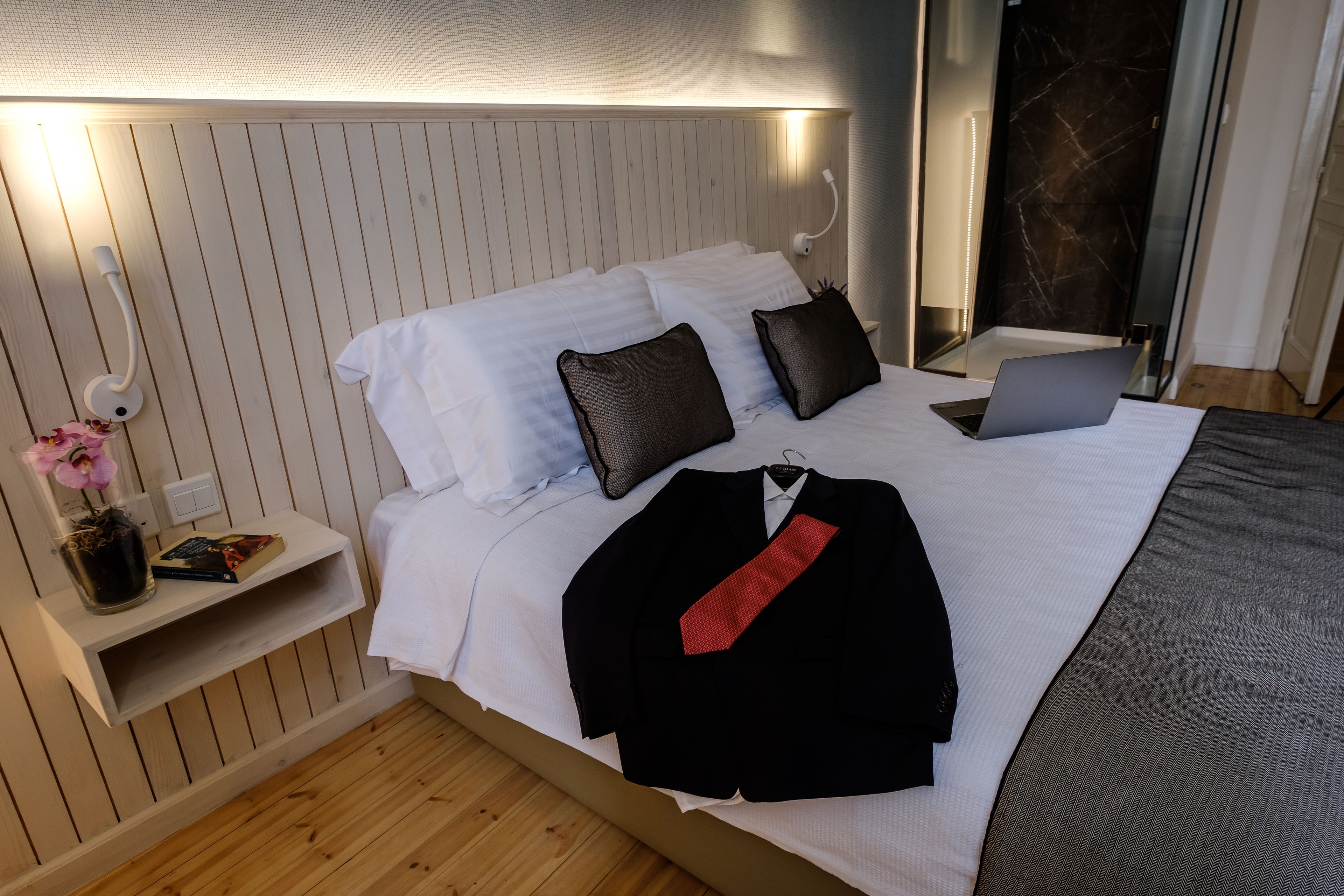 Una cama bien hecha con sábanas blancas, una computadora portátil y un traje negro sobre la cama.