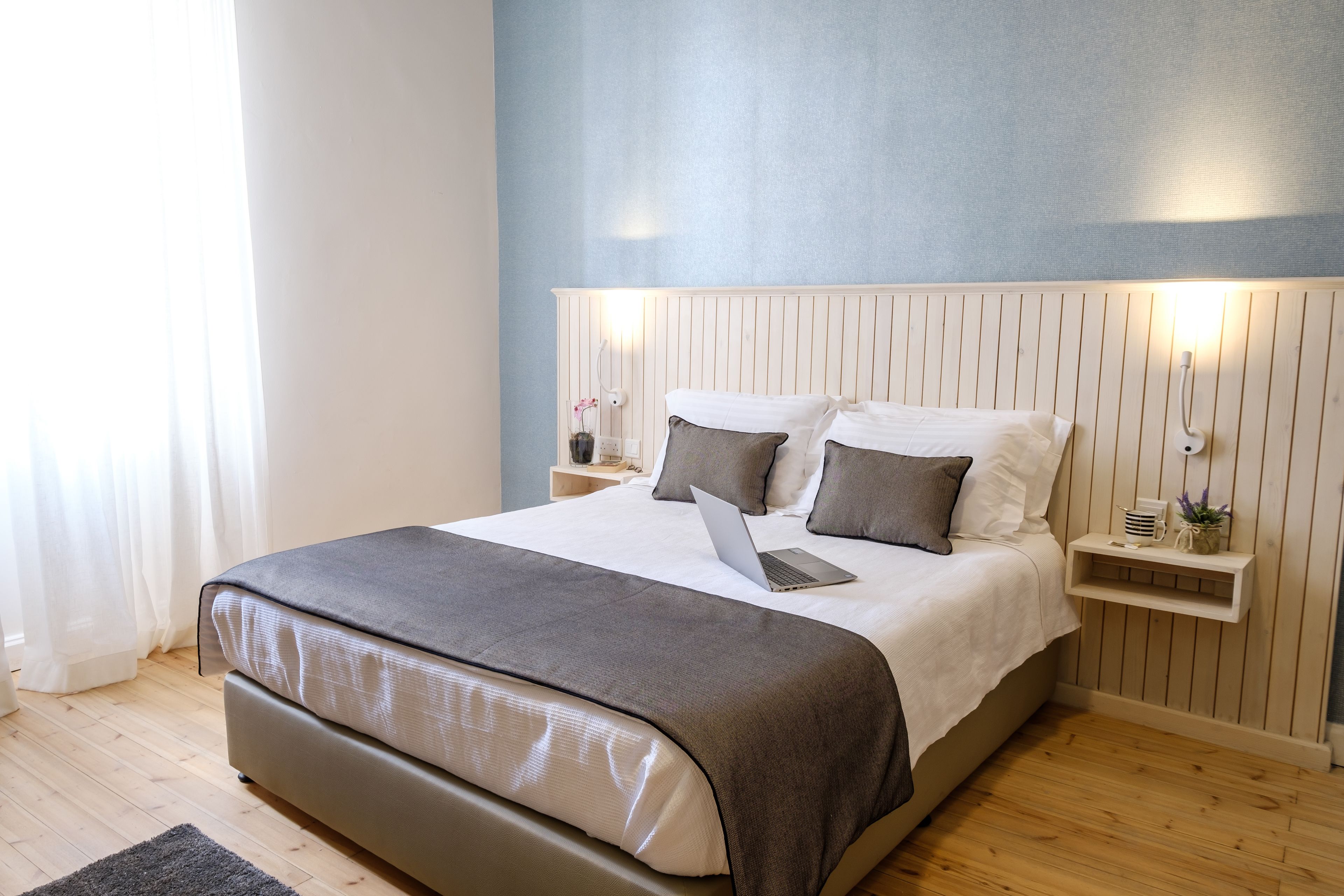 A modern bedroom with a bed, a laptop, bedside tables, and a nightstand.