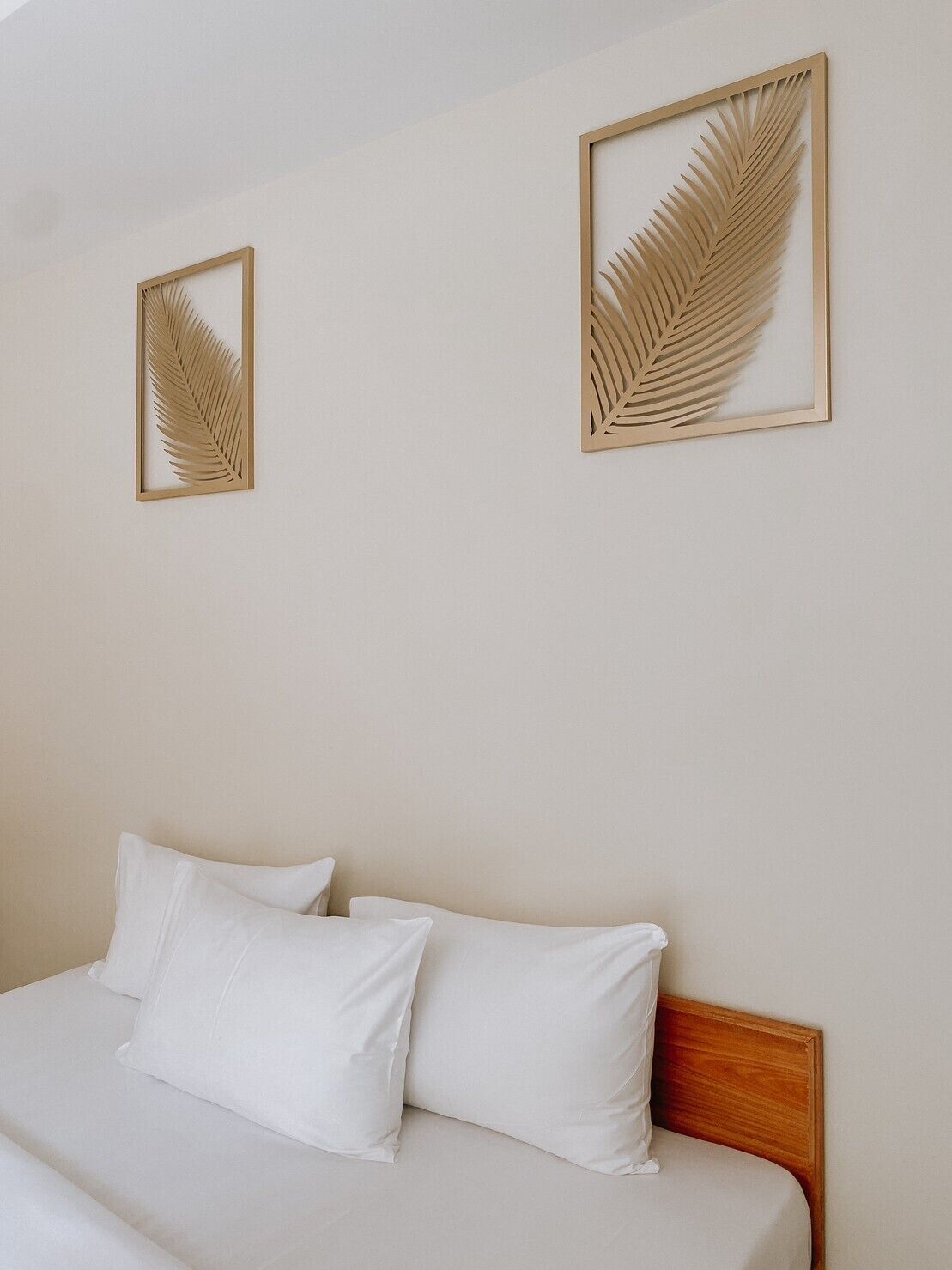 Ein Schlafzimmer mit einem Bett, zwei Kissen und zwei gerahmten Wandbildern mit Blättern.