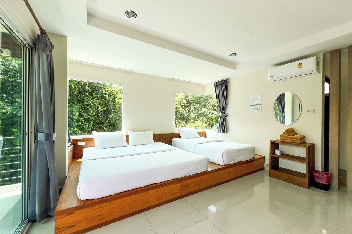 Quarto de hotel moderno com uma cama grande, cabeceira de madeira, mesa de cabeceira pequena, um espelho e vista para o verde lá fora.