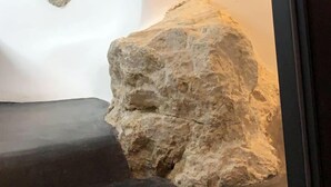 A room with a large rock centerpiece, a small stone on the floor, and a framed artwork on the wall. - The Luna Suites (Santorini)