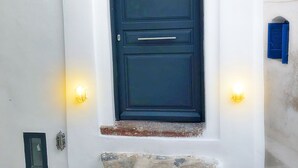 A white building with a dark blue door, stone steps, and two wall-mounted lights. - The Luna Suites (Santorini)