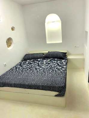 A modern bedroom with a bed, a wall-mounted light, and decorative wall features. - The Luna Suites (Santorini)