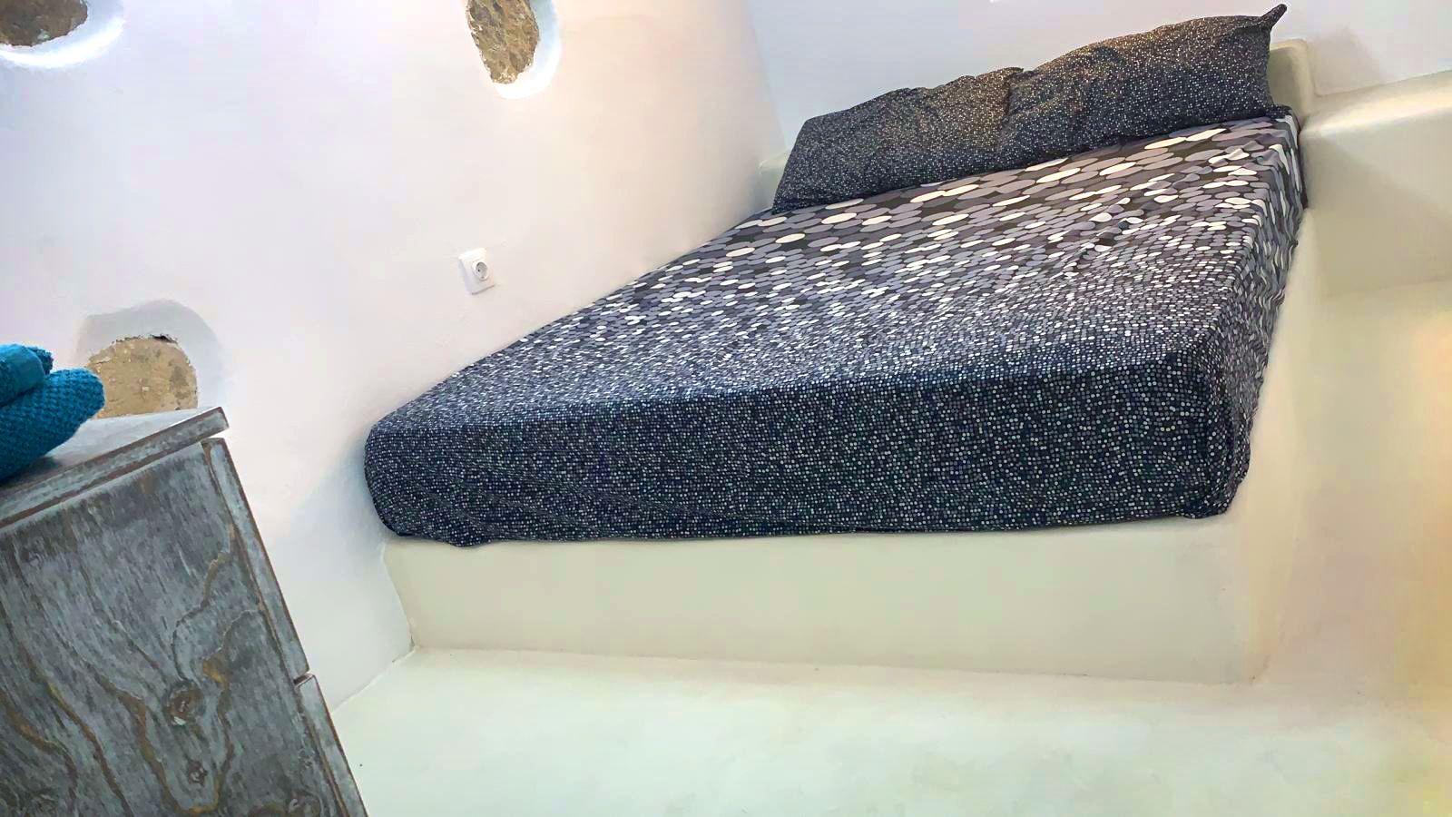 A small, cozy room with a bed, a nightstand, and a wall-mounted light fixture.