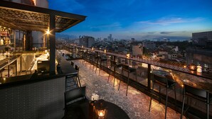 Un bar situé sur le toit d’un immeuble, offrant une vue sur la ville, avec des places assises en plein air et un sol à motifs.