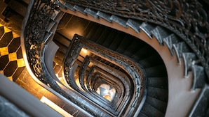 Un escalier en colimaçon orné de rampes en métal ouvragé et doté d’un motif de carreaux sur le sol.