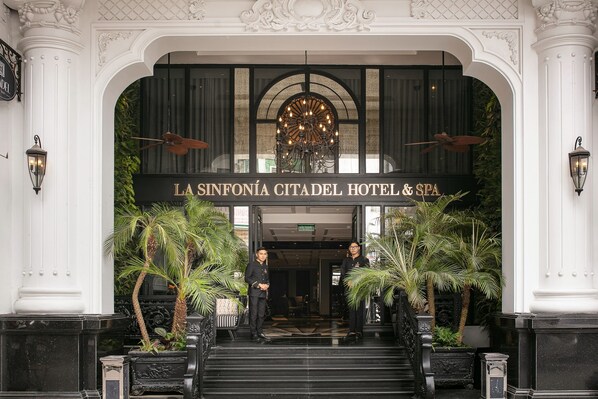 Der Eingang des La Sinfonía Citadel Hotel & Spa mit einem monumentalen Bogen, einer Kristallleuchter und Palmen.
