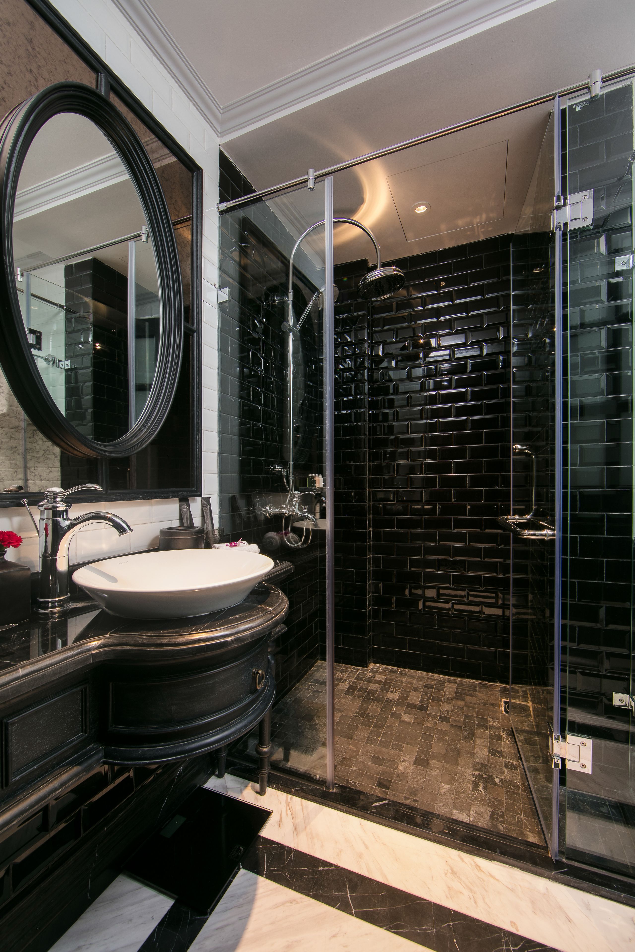 A modern bathroom with a black tiled shower, a glass-enclosed walk-in shower, and a large oval mirror.