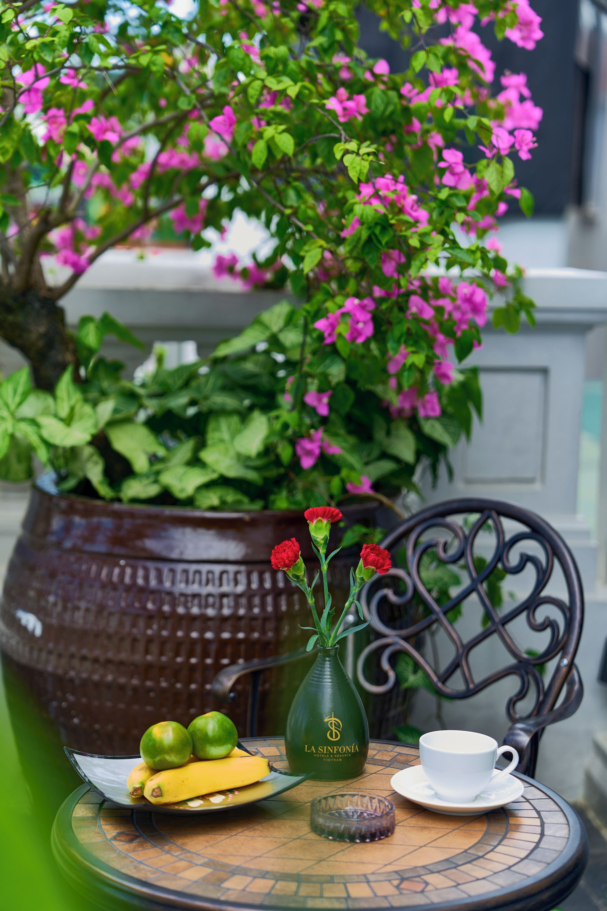 Une table avec une assiette de fruits, une tasse et un vase rempli de fleurs.